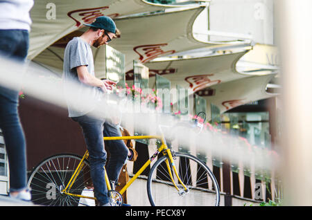 September 22, 2018 Minsk, Weißrussland: Junger Mann stand mit gelben fixie Bike im Stadtbild und macht Hand-roll Zigarette Stockfoto