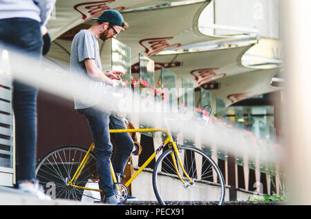 September 22, 2018 Minsk, Weißrussland: Junger Mann stand mit gelben fixie Bike im Stadtbild und macht Hand-roll Zigarette Stockfoto