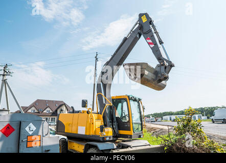 Gelber Bagger gegen Sunny bewölkter Himmel während der Straßenbau und Instandsetzung Asphalt funktioniert Stockfoto