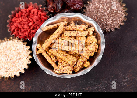 Verschiedene superfoods in kleine Schüssel in der Nähe von Müsli auf schwarzem Hintergrund. Superfood, Chia, rohen Kakaobohne, Goji, Haferflocken. Kopieren Sie Platz. Flach. Stockfoto