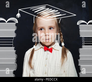 Überrascht kind Schulmädchen mit Stapel von Büchern und Promotion hat neben dem Schwarzen Brett Stockfoto