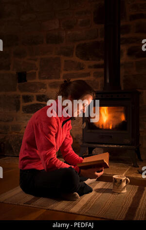 Eine Frau mit einem Buch vor einem Kaminofen. Stockfoto