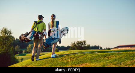 Glückliches Paar tragen Golf Outfits beim Tragen Ständer Taschen Stockfoto