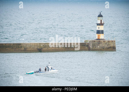 Kleines Boot an der Mündung des Seaham Hafen mit dem Leuchtturm hinter Stockfoto