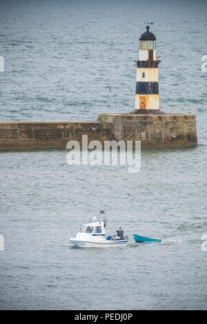 Kleines Boot an der Mündung des Seaham Hafen mit dem Leuchtturm hinter Stockfoto