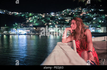 Ein Mädchen trägt ein rotes Kleid starrt mit ihrer Hand ihren Kopf in Richtung Ägäis Holding, in der Insel Astypalea, Griechenland, im Sommer in der Nacht t Stockfoto