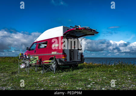 Estland - August 2018: VW Transporter T4 auf Ostsee mit Sonnenuntergang im Hintergrund und blauen Himmel mit Wolken. Im Vordergrund, Camping Ausrüstung ist eingestellt Stockfoto