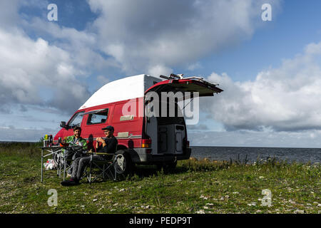 Estland - August 2018: VW Transporter T4 auf Ostsee mit Sonnenuntergang im Hintergrund und blauen Himmel mit Wolken. Im Vordergrund, Camping Ausrüstung ist eingestellt Stockfoto