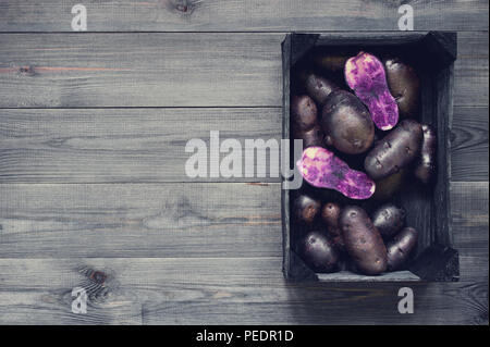 Schwarze hölzerne Hintergrund mit frischen, rohen violetten Kartoffeln, Kopie Raum Stockfoto
