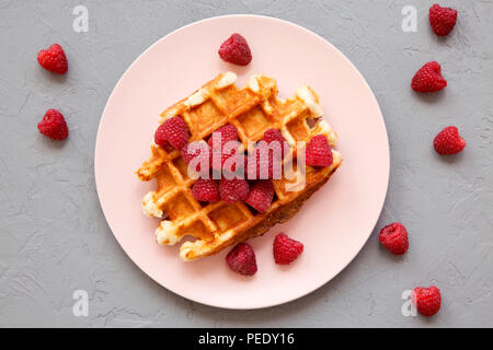 Traditionelle belgische Waffeln mit Himbeeren auf rosa Platte über graue Oberfläche, Ansicht von oben. Von oben, flach. Stockfoto