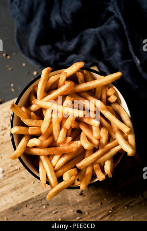 High Angle Shot einige leckere Pommes frites in eine weiße keramische Schüssel serviert, auf einem dunkelgrauen rustikalen Holztisch gelegt Stockfoto