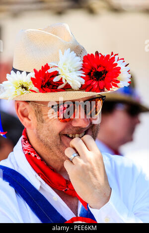 Traditionelle englische Volkstänzer aus dem Osten Kent Morris Seite. Nahaufnahme des Gesichts, Stoppel- und trägt eine Sonnenbrille, Hut mit roten und weißen Blumen. Lächeln Stockfoto