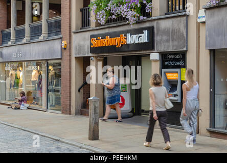 Chester, UK: Aug 6, 2018: die Menschen gehen vorbei an Lokalen mit Sainsburys store in der Innenstadt von Chester. Stockfoto