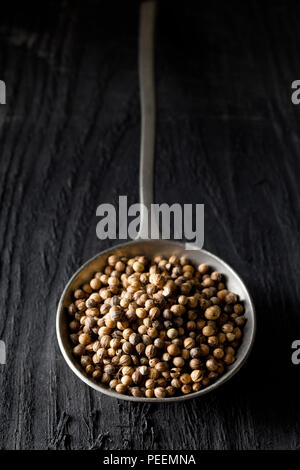 Rohe, unbearbeitete Bio Koriander oder koriander Samen in Metalllöffel auf dunklen Holztisch Stockfoto