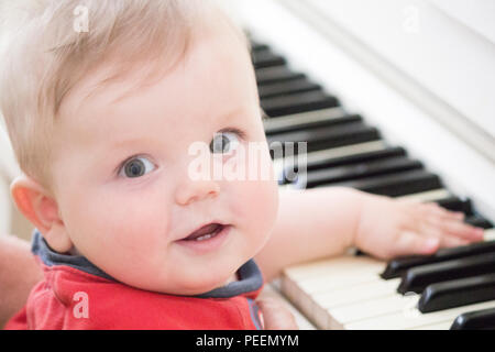 Baby am Klavier spielt in einem roten T-Shirt Stockfoto