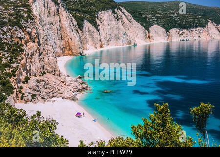 Erstaunlich Fteri Beach Lagoon, Kefalonia, Griechenland. Touristen unter dem Dach Chill in der Nähe von blauen Smaragd türkis Meer Wasser entspannen. Cliff rock Küste im Hintergrund Stockfoto