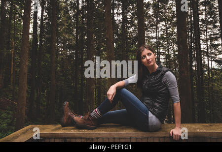 Vintage Style Foto einer jungen Frau in die Wanderstiefel sitzen auf einem Geländer in den Wald. Stockfoto