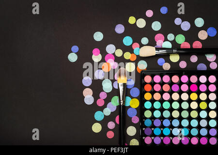 Make-up-Pinsel, Lidschatten Palette mit bunten Konfetti auf schwarzem Hintergrund. Stockfoto