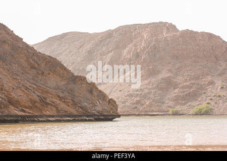 Yiti Muscat Oman Strand an einem sonnigen Tag mit dem trüben Wetter in Bergen im Hintergrund Stockfoto