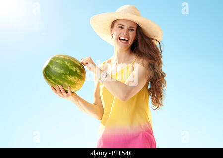 Lächelnd passende Frau in Buntes Kleid Tippen auf Wassermelone gegen den blauen Himmel Stockfoto