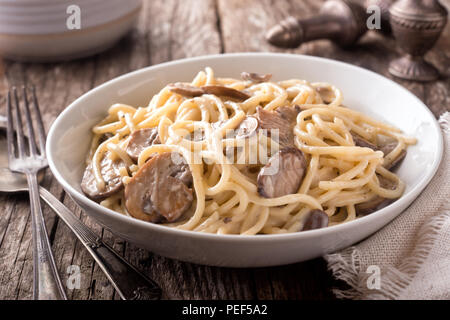 Eine Schüssel leckere Pasta Alfredo mit Pilzen auf einem rustikalen Tisch. Stockfoto