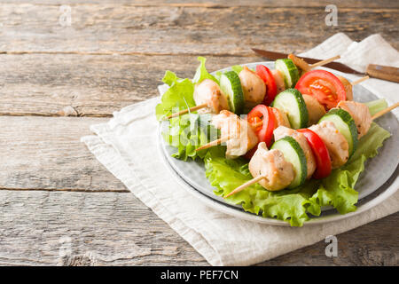 Traditionelle chicken Kebab auf Holzspieße mit Tomaten, Gurken und frischen Kräutern auf einem Teller. Stockfoto