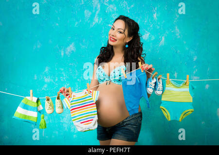 Gerne schwangere Frau hängende Kleidung für die Zukunft Baby. Warten auf das Baby. Pin up Stil Stockfoto