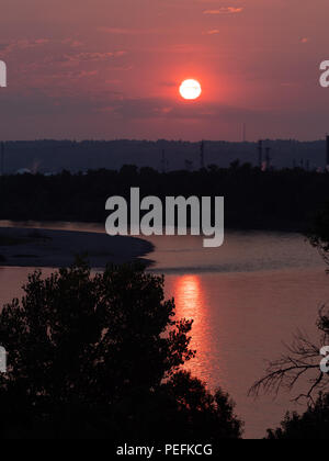 Rot, Rosa und Lila sunrise mit der Sonne in einem städtischen Gebiet. Die Verschmutzung durch den Rauch von Waldbränden ist ein dramatischer Sonnenaufgang. Stockfoto