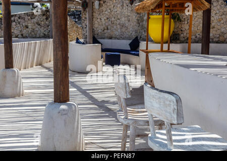 Im mediterranen Stil in Gelb, Weiß und Blau mit rustikalen Zweig Decke mit gestreiften Schatten über Sofas und Kissen, Holzböden Stockfoto