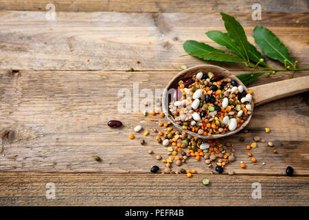 Gesunde Ernährung Konzept. Sortiment von Leguminosen in einem Stieltopf und verschüttete auf einer hölzernen Tischplatte Hintergrund, kopieren. Stockfoto