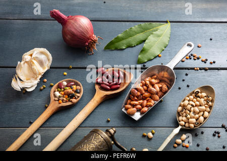 Gesunde Ernährung Konzept. Blick von oben auf die Wohnung der Sortiment von Leguminosen auf schwarze hölzerne Tischplatte Hintergrund legen, Schaufel und Pfannen und reibe. Stockfoto
