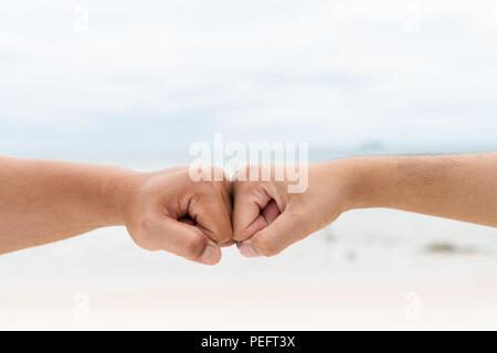 Männer Hände Faust zusammen Anstoßen auf unscharfen Meer und Himmel Hintergrund. Friendship Day Konzept. Stockfoto