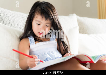 Glücklich süsse kleine Mädchen lächelnd und mit roten Bleistift und Zeichnen, Schreiben auf ein Buch, um Hausaufgaben zu machen. kid Bildung Konzept. Stockfoto