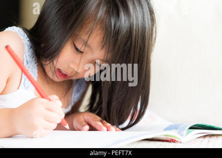 Glücklich süsse kleine Mädchen lächelnd und mit roten Bleistift und Zeichnen, Schreiben auf ein Buch, um Hausaufgaben zu machen. Stockfoto