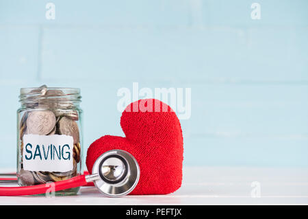 Geld sparen und Health Care Konzept. Ein Behälter enthält Münzen mit Stethoskop und handgefertigten rotes Herz auf weißem Holz- Hintergrund. Stockfoto