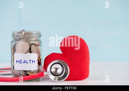 Geld sparen und Health Care Konzept. Ein Behälter enthält Münzen mit Stethoskop und handgefertigten rotes Herz auf weißen und pastellfarbenen Grün Holz- Hintergrund. Stockfoto