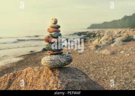 Nachhaltige Cairn unterschiedliche Formen auf dem Hintergrund der Ostsee und dem ruhigen Wald auf den felsigen Strand in hellen Pastellfarben Stockfoto