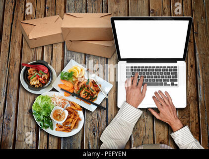 Geschäftsmann ein weißes Hemd und grün Krawatte mit der Arbeit an seinem Laptop auf rustikalen Holztisch und asiatische Küche Stockfoto