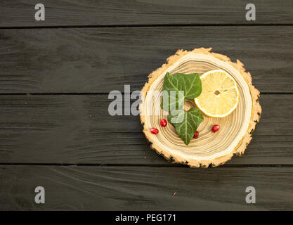 Holz mit mit Zitronenscheiben und Granatapfel Beeren auf schwarzem Hintergrund Stockfoto