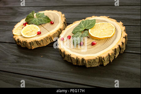Holz mit mit Zitronenscheiben und Granatapfel Beeren auf schwarzem Hintergrund Stockfoto