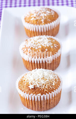 Drei hausgemachte Muffins mit Kokosnuss Pulver Weiß platte Hintergrund. Gesunde Ernährung Konzept. Stockfoto