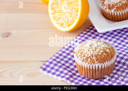 Leckere hausgemachte orange Muffins mit Kokosnuss Pulver Weiß platte Holz- Hintergrund. Gesunde Ernährung Konzept. Selektive konzentrieren. Stockfoto