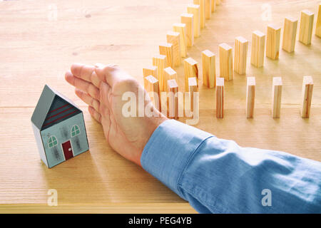 Konzept Bild von Immobilien Versicherungen und Schutz. Mann die Hände die Blockierung der Domino Effekt zu speichern, ein kleines Haus Stockfoto