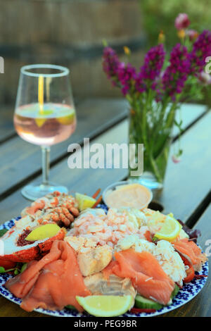 Platte mit schottischen Meeresfrüchten und Schalentieren auf einem Tisch im Freien mit einem alkoholischen Getränk und einer Vase mit wilden Orchideen Stockfoto