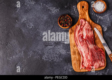 Teil der rohen Speck Streifen auf dunklem Hintergrund, Ansicht von oben. Stockfoto