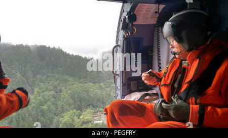 Alaska reg. Bill Walker bewertet das Ausmaß der Schäden, die durch Erdrutsche in Sitka, Alaska, bei einem Überflug an Bord eines Coast Guard Air Station Sitka MH-60 Jayhawk Helikopter August 19, 2015. Air Station Sitka Personal unterstützt mit Bewertung und Wiederherstellungsmaßnahmen und flog National Forest Service Boden und Wasser Experten, Sitka Bergrettung Personal- und Mandatsträger in den Erdrutsch Websites. (U.S. Coast Guard Foto) Stockfoto