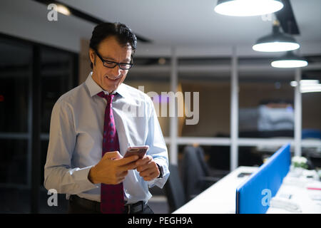 Gerne Reife Geschäftsmann mit Mobiltelefon im Büro bei Nacht Stockfoto