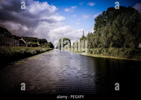 Querformat der Damse Vaart River in der Nähe der Stadt Damme im Norden Belgiens, mit der Stadt im Hintergrund und den Fluss im Vordergrund. Stockfoto