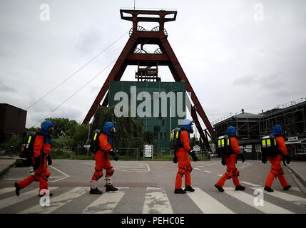 Deutschland, Herne. 18 Juni, 2018. Die Mitglieder der u-Feuerwehr Spaziergang über einen Zebrastreifen vor den Förderturm der ehemaligen Pluto Mine. An der ehemaligen Zeche Pluto, die U-Bahn Feuerwehr Züge die Rettung der Bergleute im Falle der u-Unfälle im Bergbau. Credit: Oliver Berg/dpa/Alamy leben Nachrichten Stockfoto