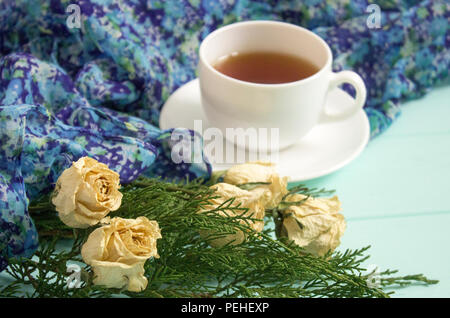 Tasse Tee mit getrockneten Rosen und Zweige von Juniper auf einem türkis Hintergrund Stockfoto
